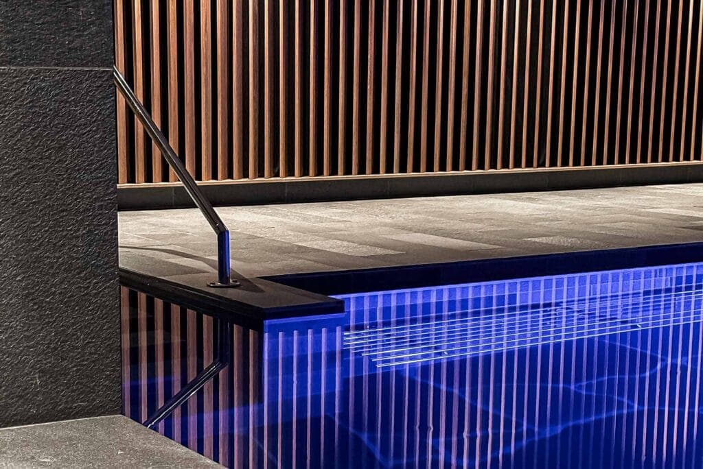 Stenklädd poolkant och träpanel vid den blå poolen på Earth Spa, Billingehus